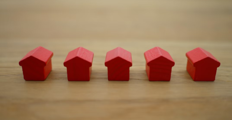 five small wooden red monopoly houses on a wooden desk.